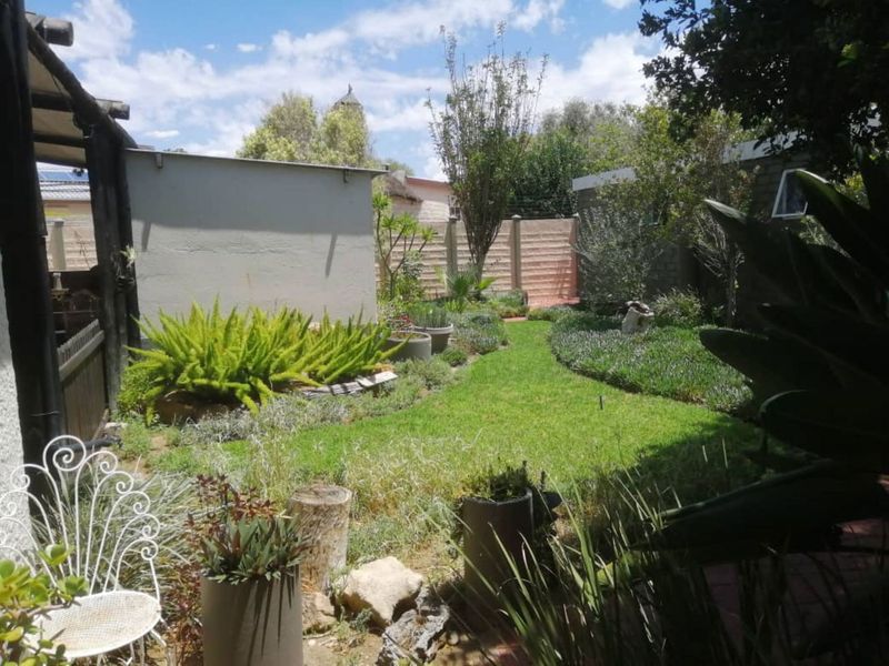 A private rear garden featuring a well-maintained lawn, established greenery, and secure perimeter boundary walling.