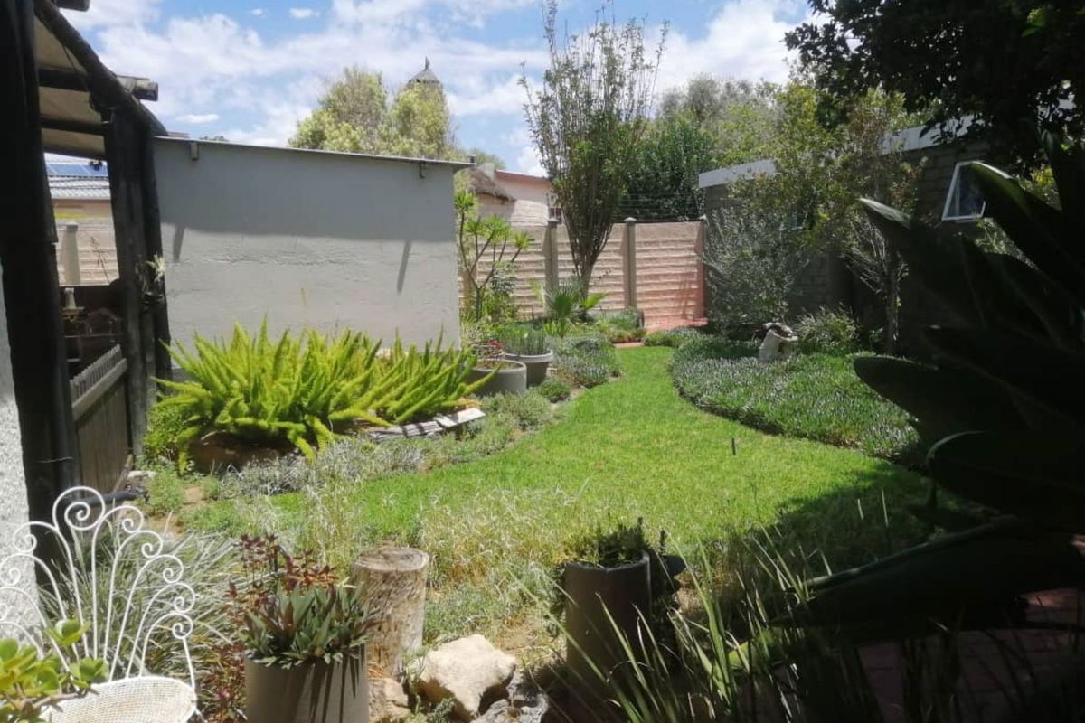 A private rear garden featuring a well-maintained lawn, established greenery, and secure perimeter boundary walling.
