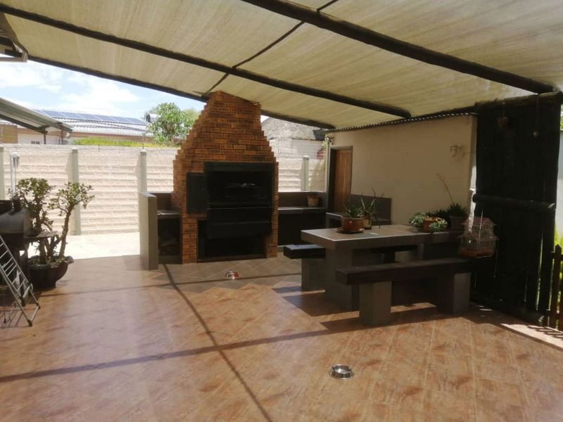 Covered outdoor patio area featuring a built-in brick braai, tiled flooring, and integrated concrete seating, ideal for outdoor entertaining.