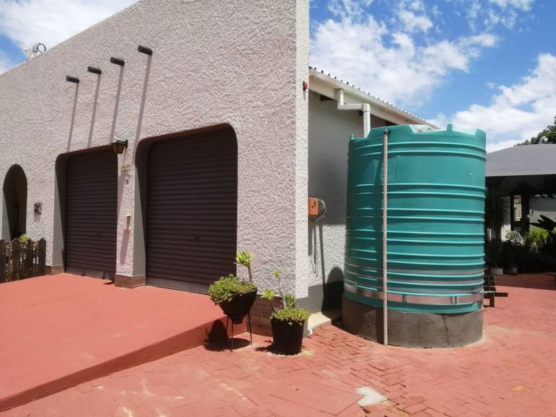 Front exterior view of the property featuring a double garage with roller shutter doors and an installed water storage tank on a paved driveway.