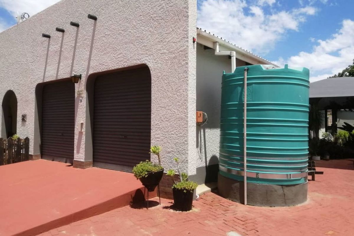 Front exterior view of the property featuring a double garage with roller shutter doors and an installed water storage tank on a paved driveway.