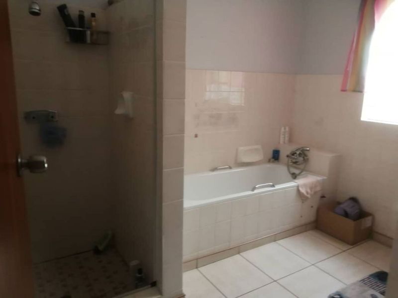 A functional bathroom featuring a built-in bathtub, a separate shower enclosure, and neutral wall and floor tiling.
