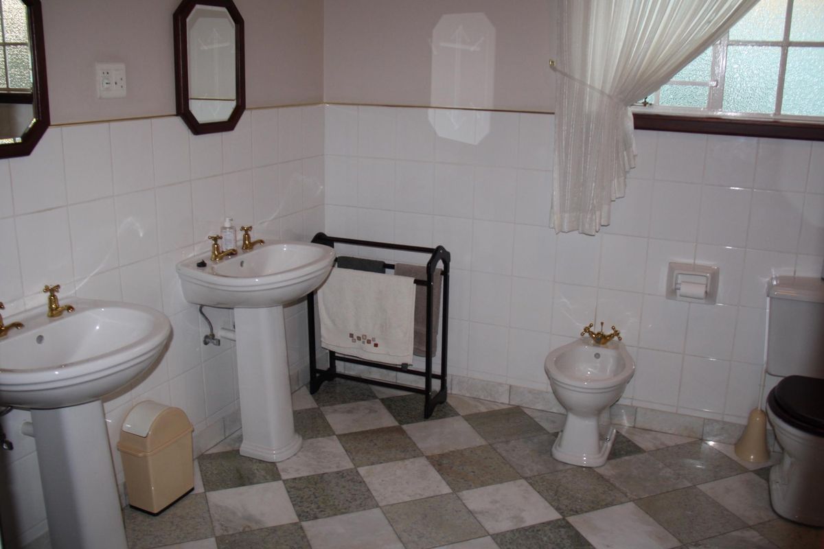 A functional bathroom featuring dual pedestal sinks, a bidet, and a toilet with classic white wall tiling and checkered floor tiles.