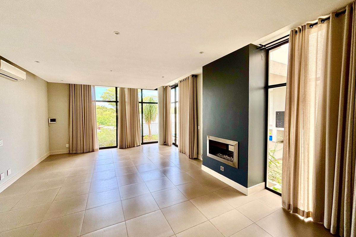 Spacious living area featuring large floor-to-ceiling windows, tiled flooring, and a modern built-in fireplace, offering abundant natural light and a seamless indoor-outdoor flow.