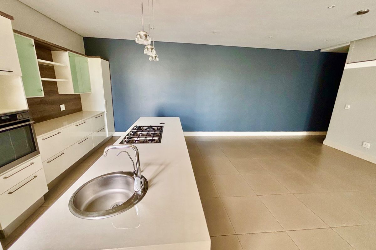 Modern open-plan kitchen featuring a central island with a built-in gas hob, stainless steel sink, and sleek cabinetry with integrated oven.