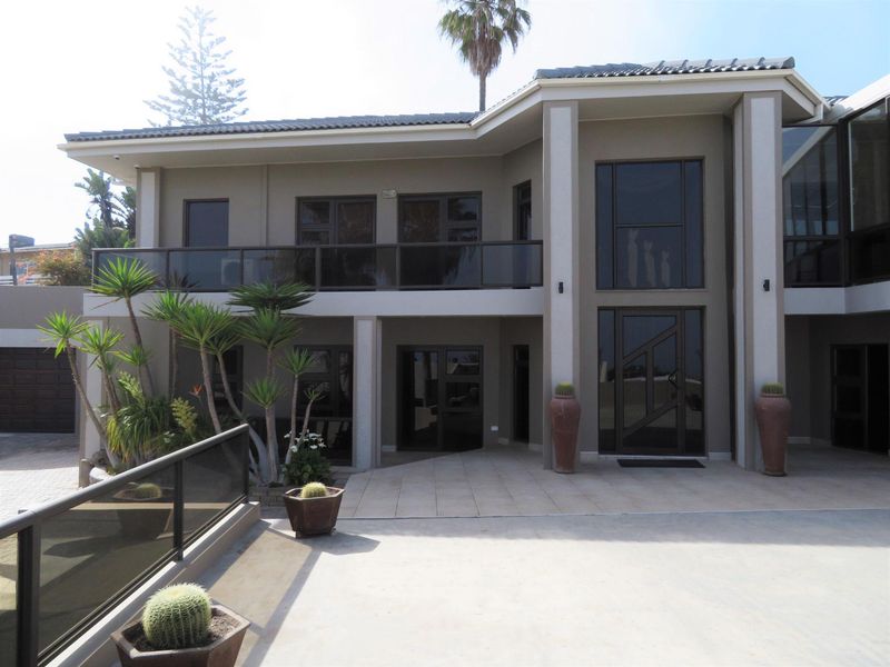 A modern two-story residential facade featuring a tiled patio, glass balustrades, and large dark-framed windows and doors.