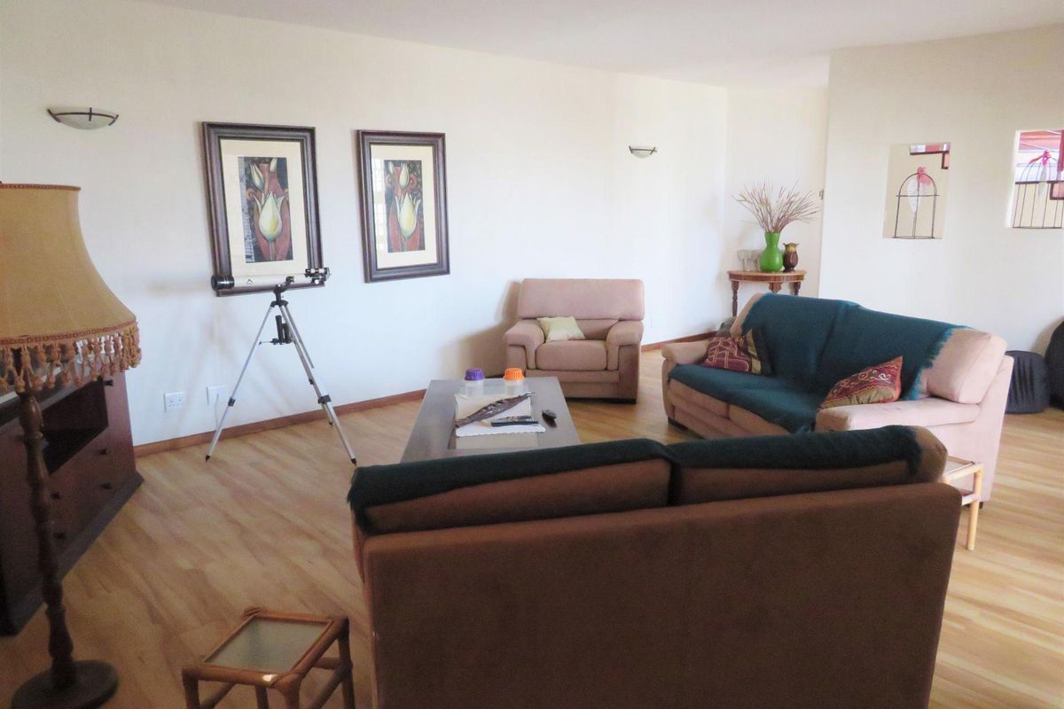 Spacious living room featuring light-toned laminate flooring and wall-mounted lighting fixtures.
