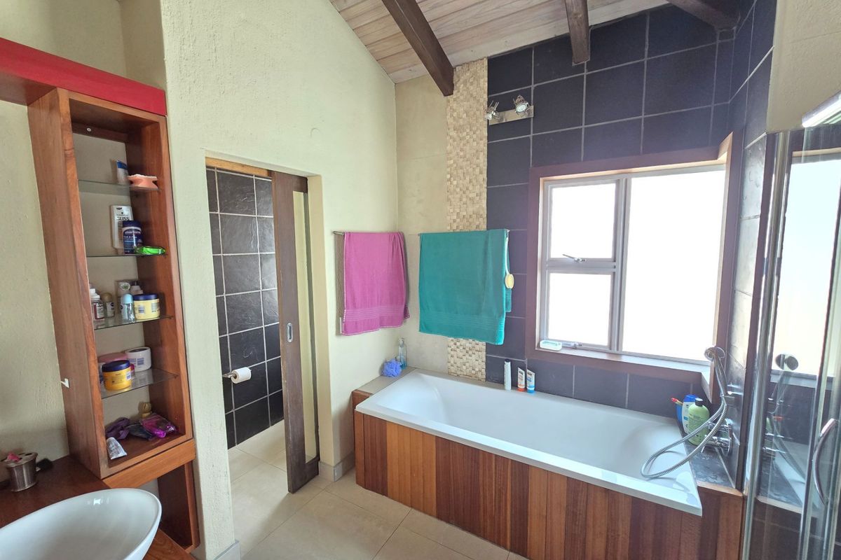 A bathroom featuring a built-in bathtub with timber paneling, exposed timber ceiling beams, tiled walls, and a separate shower area.