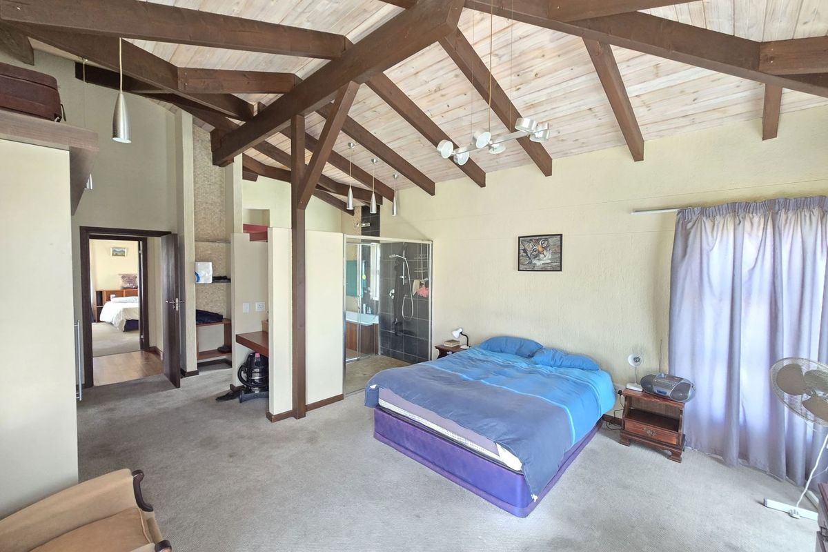 Spacious bedroom featuring high vaulted timber-beamed ceilings, integrated en-suite bathroom with glass shower enclosure, and neutral wall finishes.
