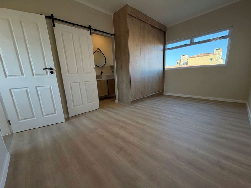 A bright, empty bedroom featuring modern laminate flooring, a built-in wardrobe, and a sliding barn door leading to an en-suite bathroom.