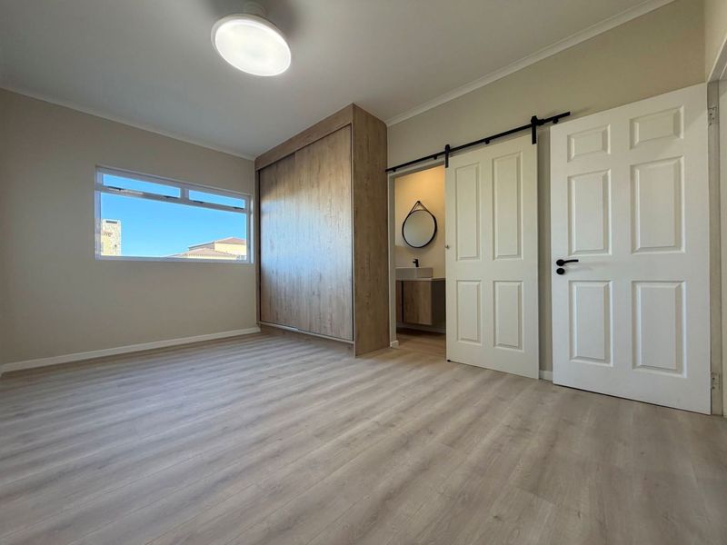 A bright, modern bedroom featuring light laminate flooring, a built-in wardrobe, and a sliding barn door leading to an en-suite bathroom.