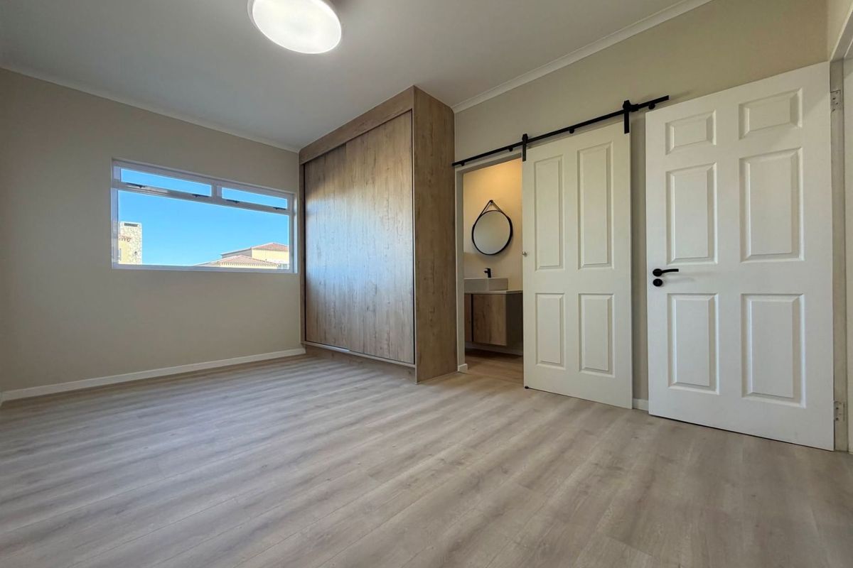 A bright, modern bedroom featuring light laminate flooring, a built-in wardrobe, and a sliding barn door leading to an en-suite bathroom.