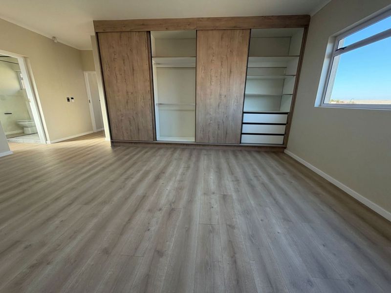 Spacious bedroom featuring modern laminate flooring and a large, integrated built-in wardrobe with ample shelving and hanging space.
