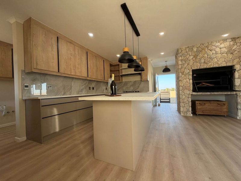 Modern open-plan kitchen featuring a central island, stone splashback, and a prominent stone-clad fireplace with a built-in braai.