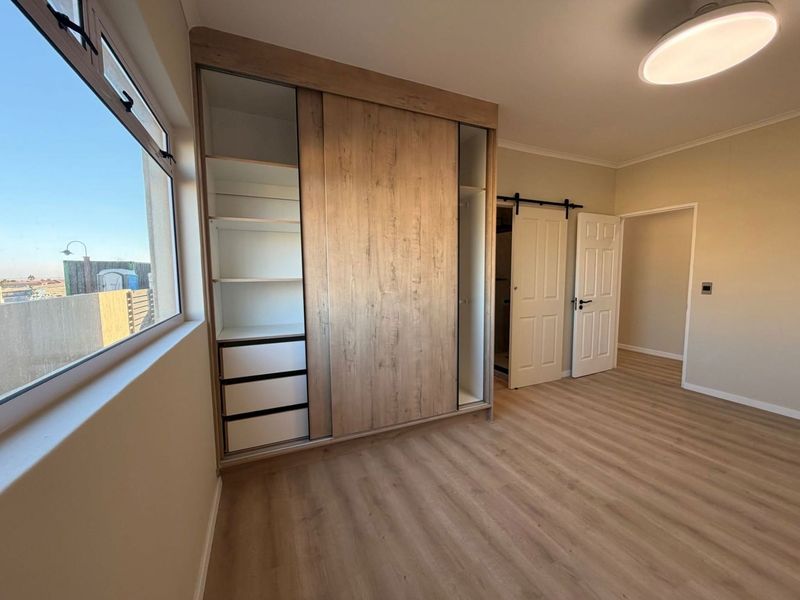 A bright, modern bedroom featuring light wood-look laminate flooring, a large built-in sliding wardrobe, and a stylish sliding barn door.
