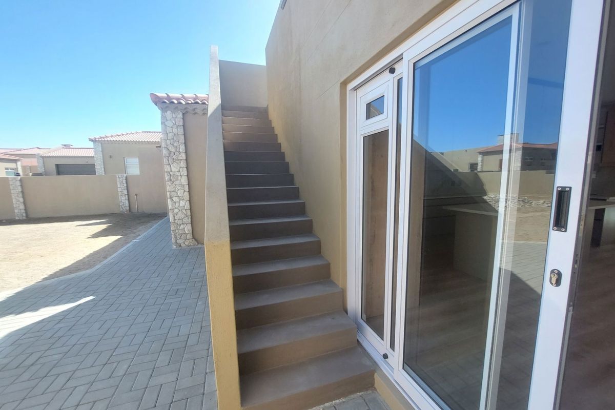 Exterior view of the property featuring a paved walkway, external staircase, and sliding glass door access to the interior.
