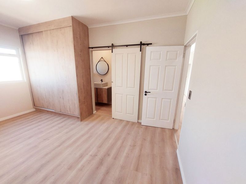 A bright bedroom featuring light wood-look flooring, a large built-in wardrobe, and a sliding barn door leading to an en-suite bathroom.