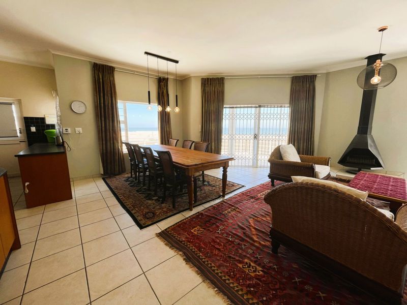 Spacious open-plan living and dining area featuring tiled floors, a modern freestanding fireplace, and direct access to a patio with ocean views.