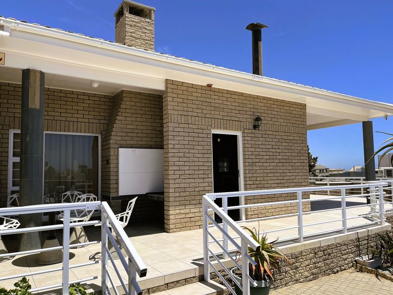 A spacious covered patio featuring a built-in braai, brick facade, and white metal balustrades, offering a functional outdoor entertainment area.