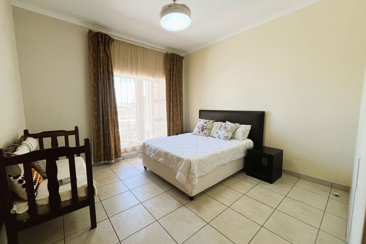 A spacious bedroom featuring tiled flooring, a ceiling fan, and a sliding glass door providing access to the exterior.