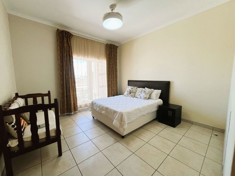 A spacious bedroom featuring tiled flooring, a ceiling fan, and a sliding glass door providing access to the exterior.