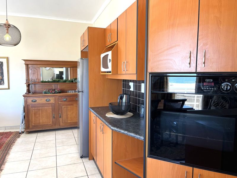 Kitchen featuring wood-look laminate cabinetry, built-in oven and microwave, dark tiled splashback, and light ceramic floor tiles.