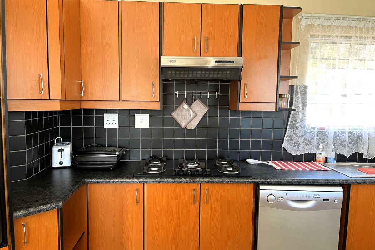 A functional kitchen featuring wood-look laminate cabinetry, dark tiled backsplash, gas hob with extractor fan, and a stainless steel sink.