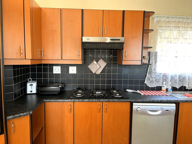 A functional kitchen featuring wood-look laminate cabinetry, dark tiled backsplash, gas hob with extractor fan, and a stainless steel sink.