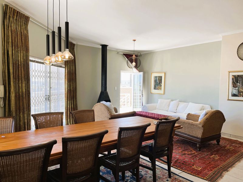 Spacious open-plan living and dining area featuring a modern freestanding fireplace, tiled flooring, and direct access to an outdoor balcony through sliding security doors.