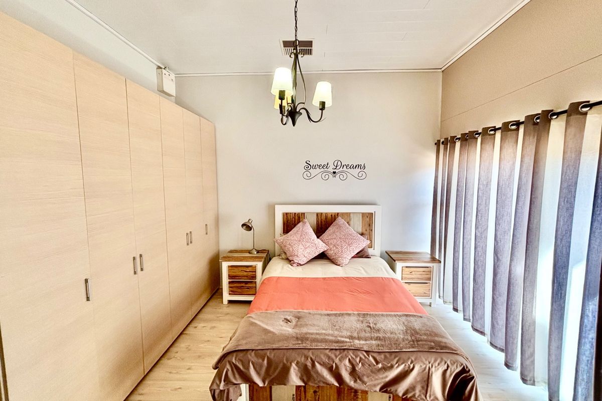 A well-maintained bedroom featuring extensive built-in light wood cabinetry, laminate flooring, and a central chandelier.