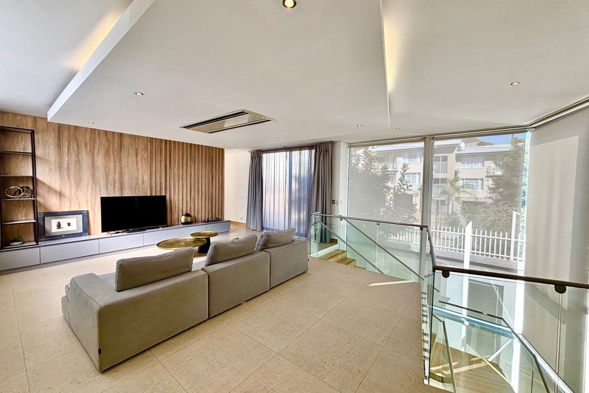 Modern open-plan living area featuring a feature wood-panelled wall, recessed ceiling lighting, ducted air conditioning, and a glass-railed staircase.