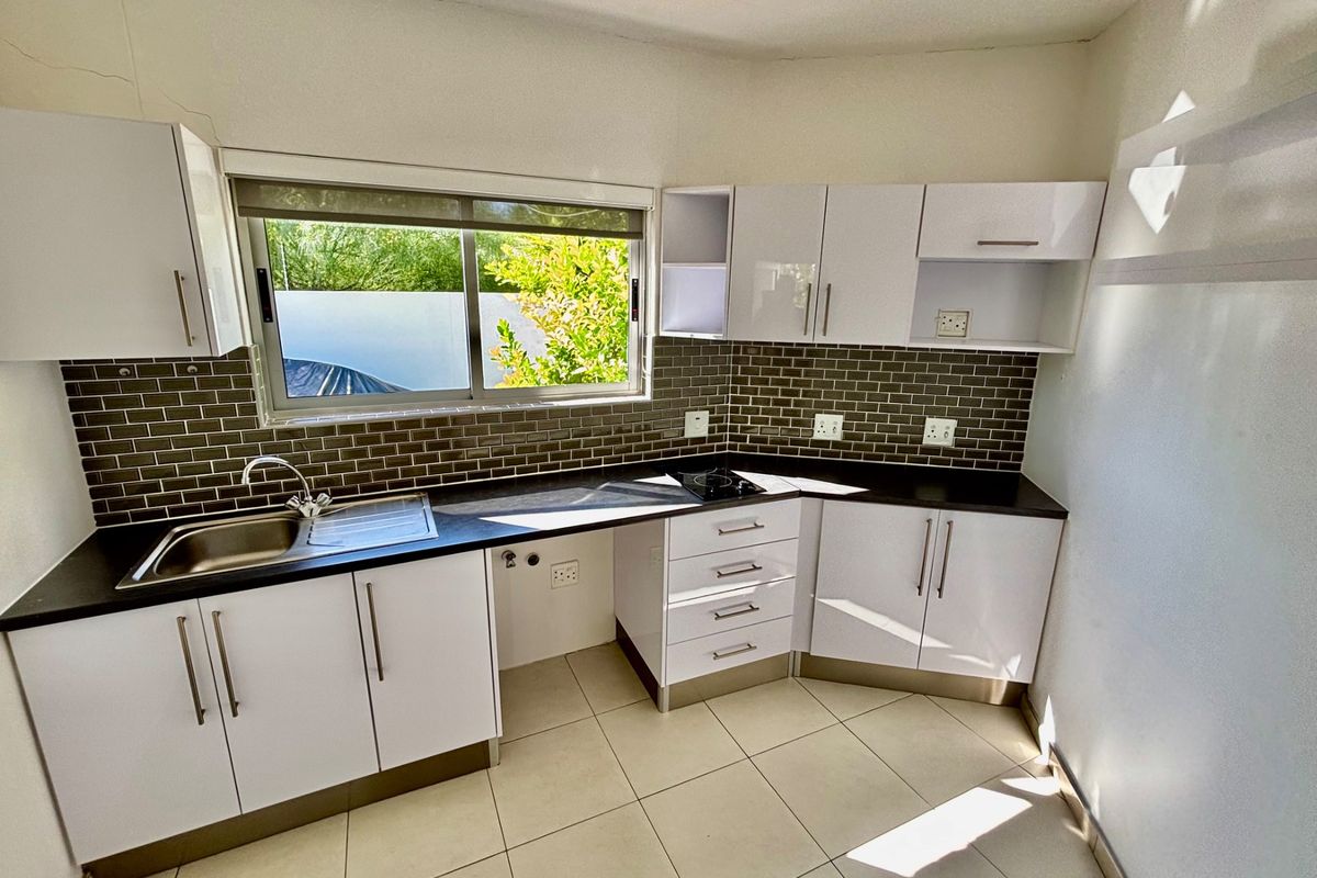 Modern kitchen featuring white cabinetry, dark countertops, subway tile backsplash, stainless steel sink, and built-in cooktop.