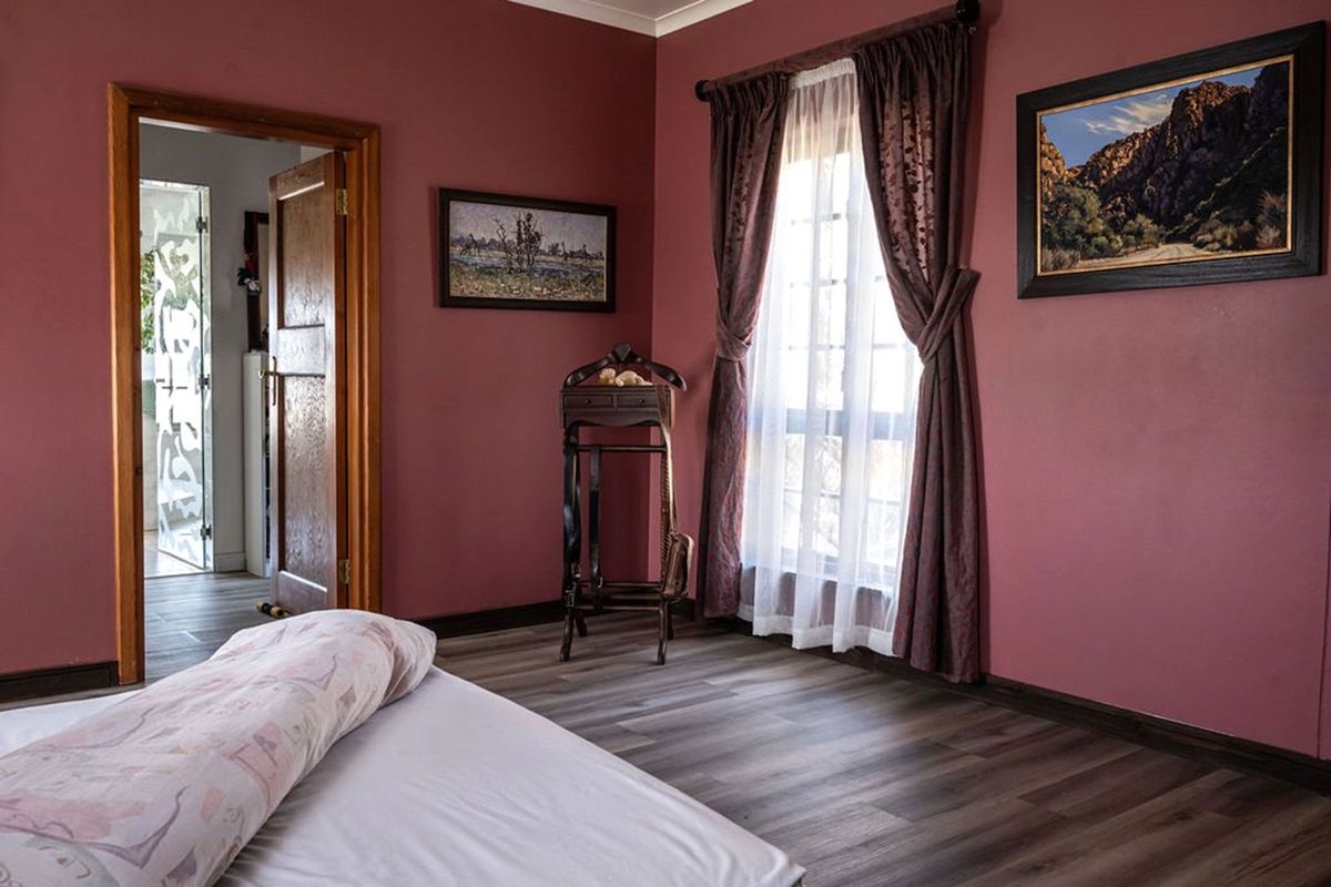 A bedroom featuring wood-look laminate flooring, a window with curtains, and a wooden door frame leading to an adjacent room.