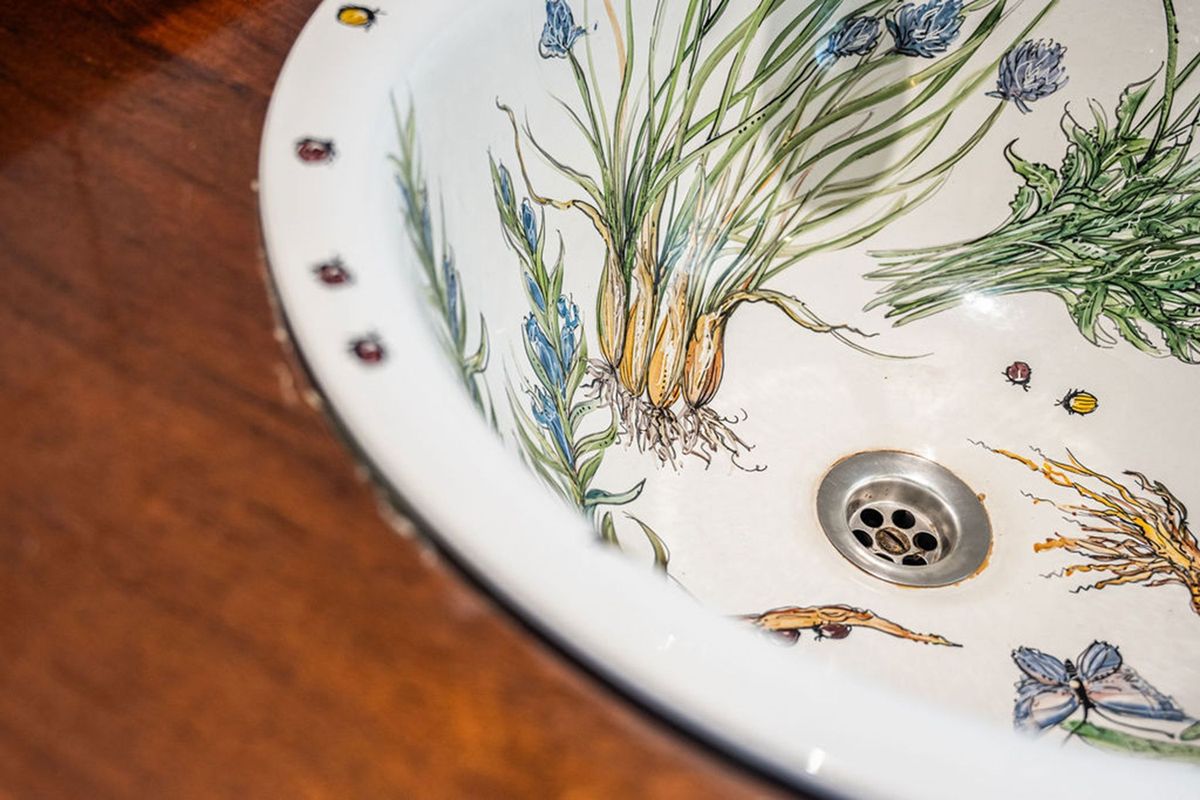 A decorative ceramic basin with botanical illustrations set into a wooden countertop.