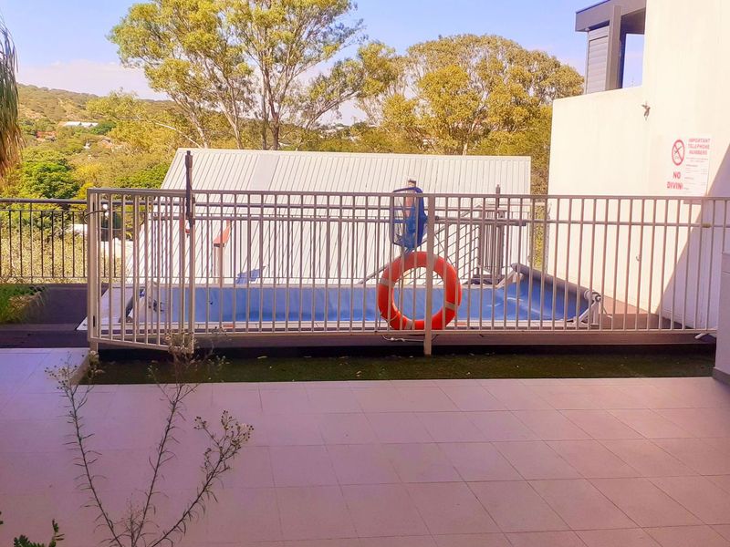 An outdoor patio area featuring a swimming pool with safety fencing and a built-in sink, overlooking a scenic landscape.
