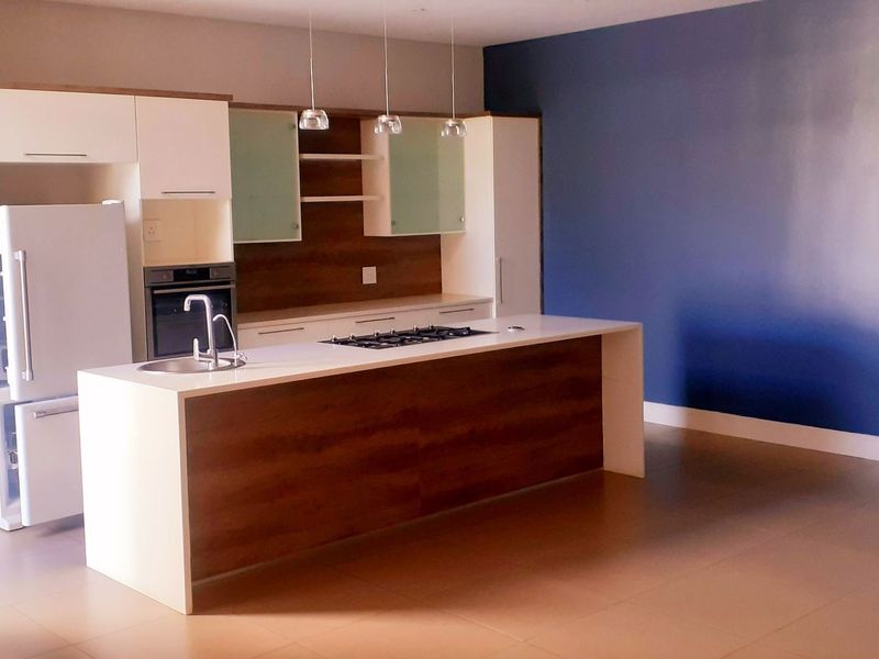 Modern open-plan kitchen featuring a central island with a gas hob, built-in oven, and sleek cabinetry, set against a bold blue accent wall.