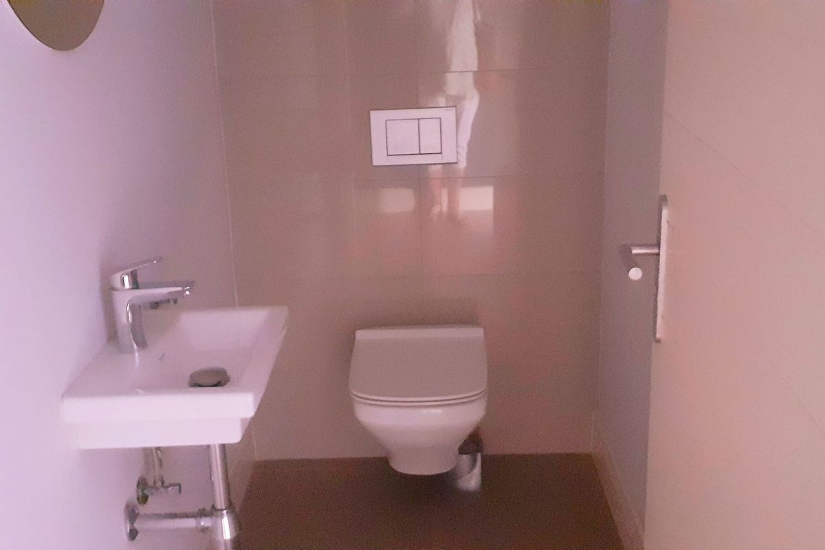 A compact, modern powder room featuring a wall-mounted toilet and a minimalist wall-mounted basin with chrome fixtures.