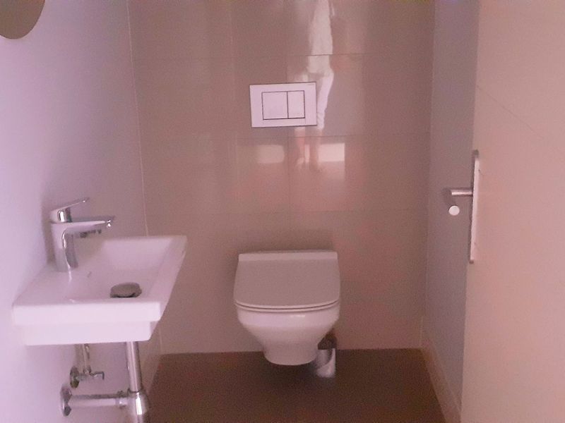 A compact, modern powder room featuring a wall-mounted toilet and a minimalist wall-mounted basin with chrome fixtures.