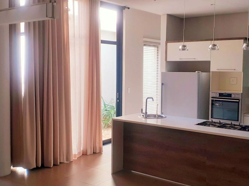 Modern open-plan living area featuring a contemporary kitchen with a central island, built-in appliances, and large glass doors leading to an outdoor space.