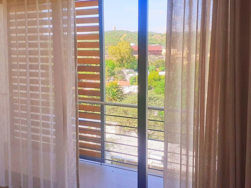 A bright balcony area featuring a metal balustrade, sliding glass doors, and external louvre shutters, offering a pleasant view of the surrounding neighborhood.