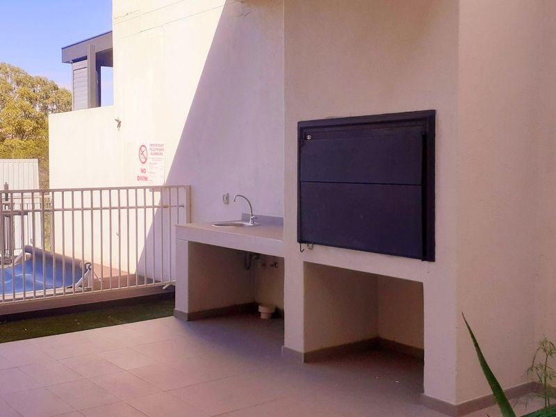 Covered patio area featuring a built-in braai, integrated sink, and tiled flooring, overlooking the pool area.