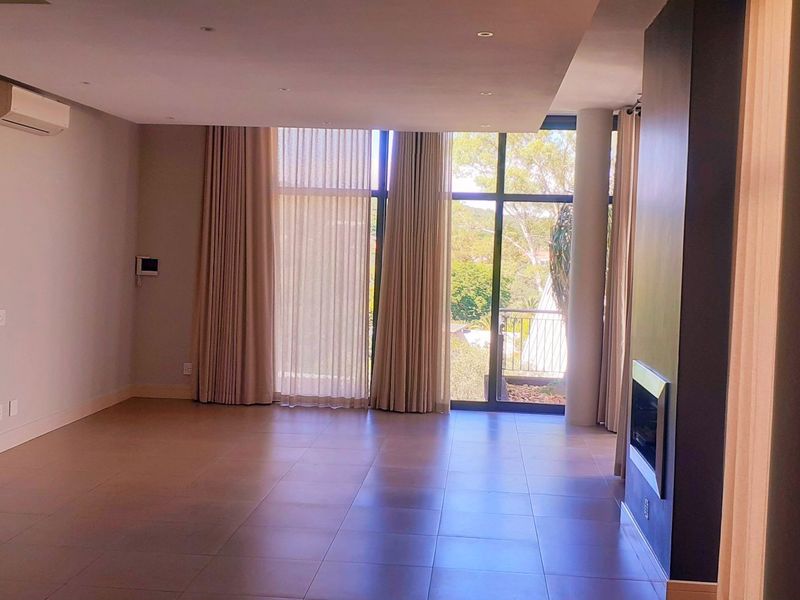 Spacious, modern living area featuring large floor-to-ceiling windows, tiled flooring, a built-in fireplace, and a wall-mounted air conditioning unit.