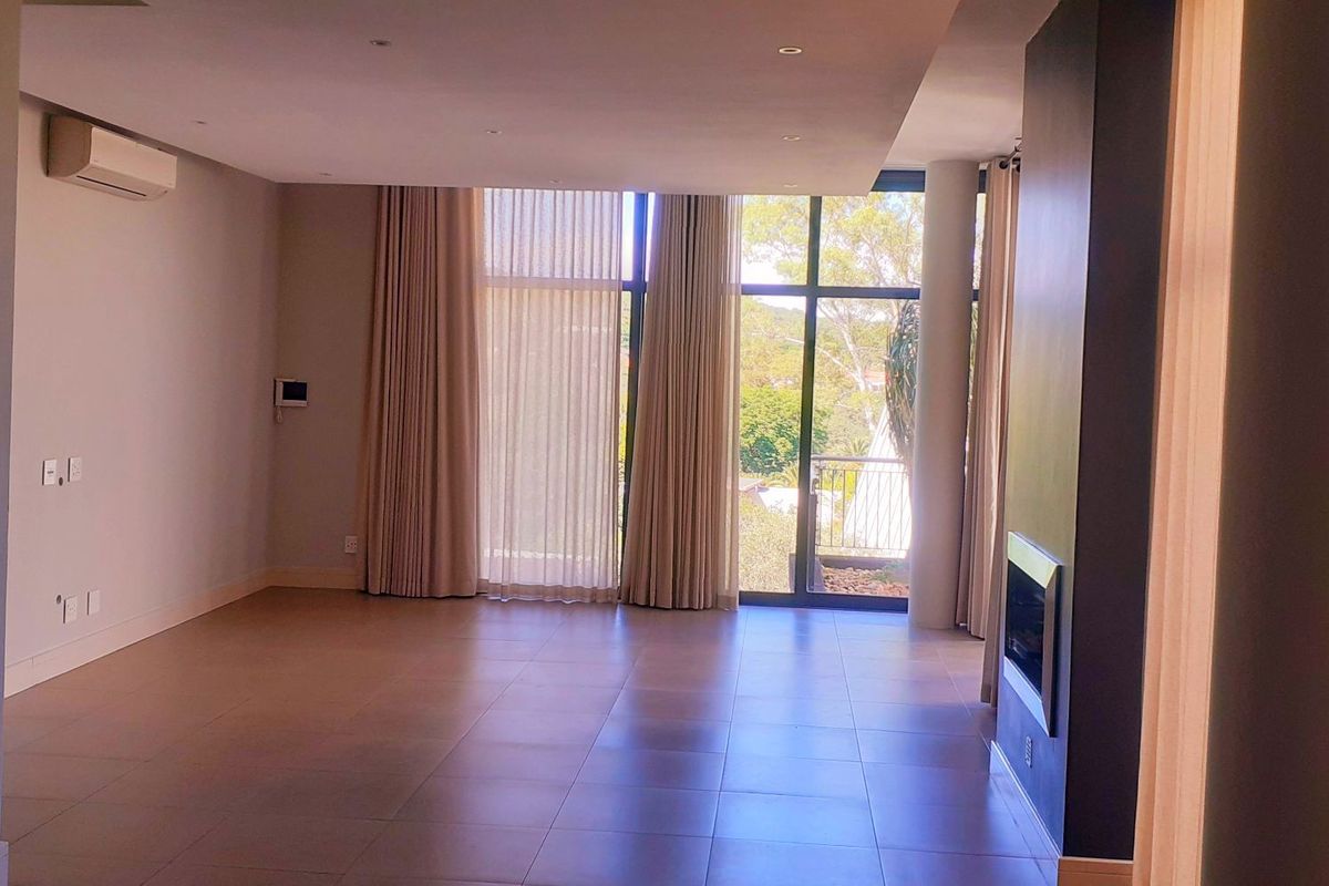 Spacious, modern living area featuring large floor-to-ceiling windows, tiled flooring, a built-in fireplace, and a wall-mounted air conditioning unit.