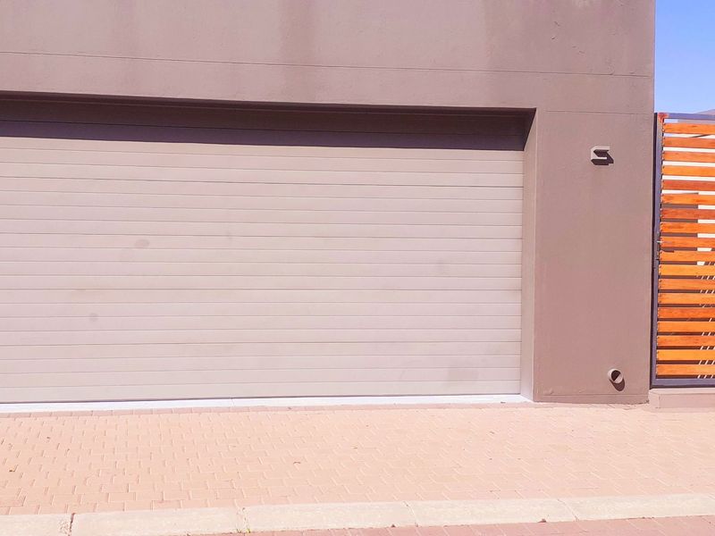 Modern townhouse garage facade featuring a clean sectional door, adjacent timber pedestrian gate, and decorative stone cladding detail.