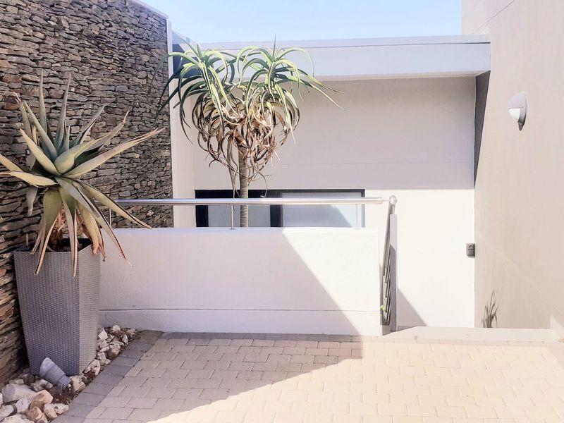 A modern outdoor patio area featuring a textured stone feature wall, paved flooring, and a sleek stainless steel balustrade.