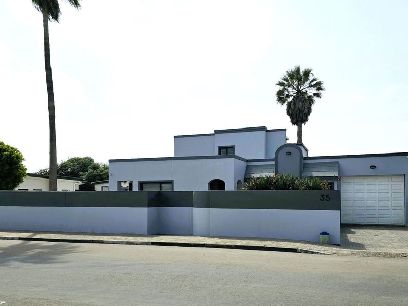 Front elevation of a modern house featuring a clean facade, secure boundary wall, and a paved driveway leading to a single garage.