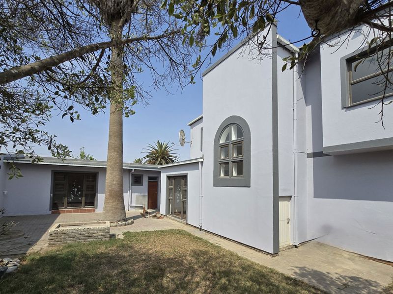 Rear exterior view of the house featuring a paved patio area, a brick planter, and a large palm tree in the garden.