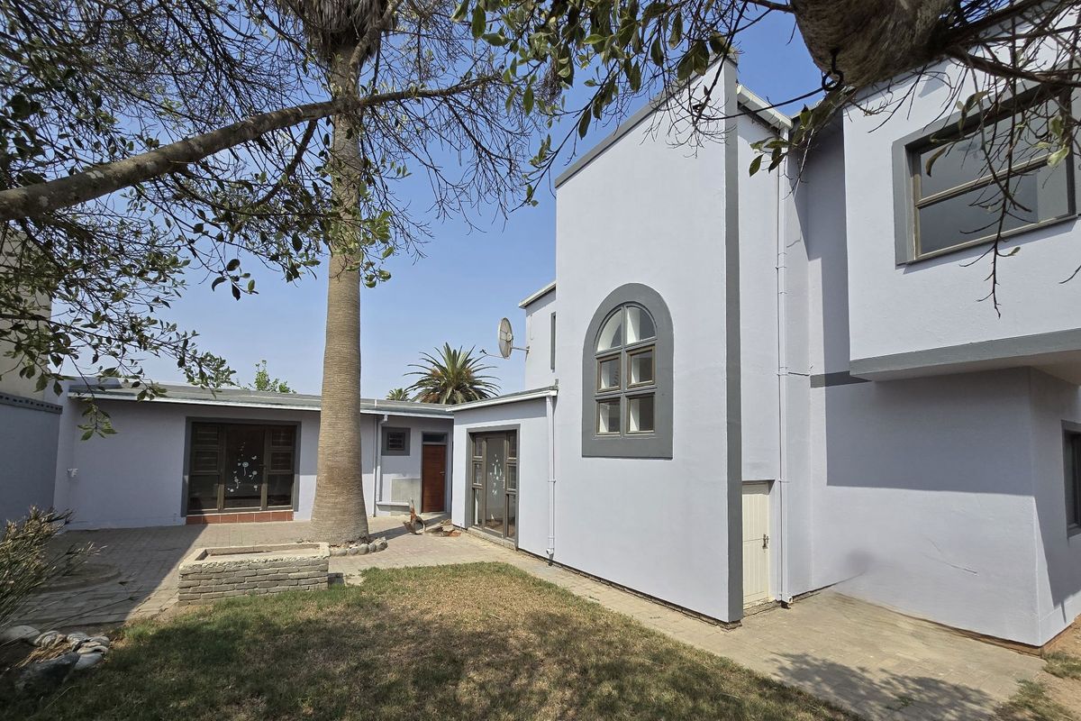 Rear exterior view of the house featuring a paved patio area, a brick planter, and a large palm tree in the garden.