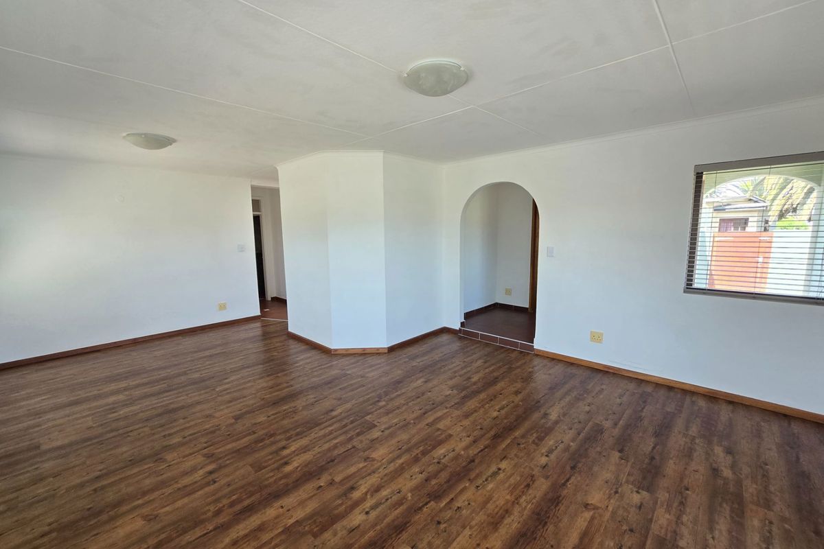 Spacious, empty living area featuring wood-look laminate flooring, arched doorway, and neutral white walls, providing a versatile blank canvas for interior design.