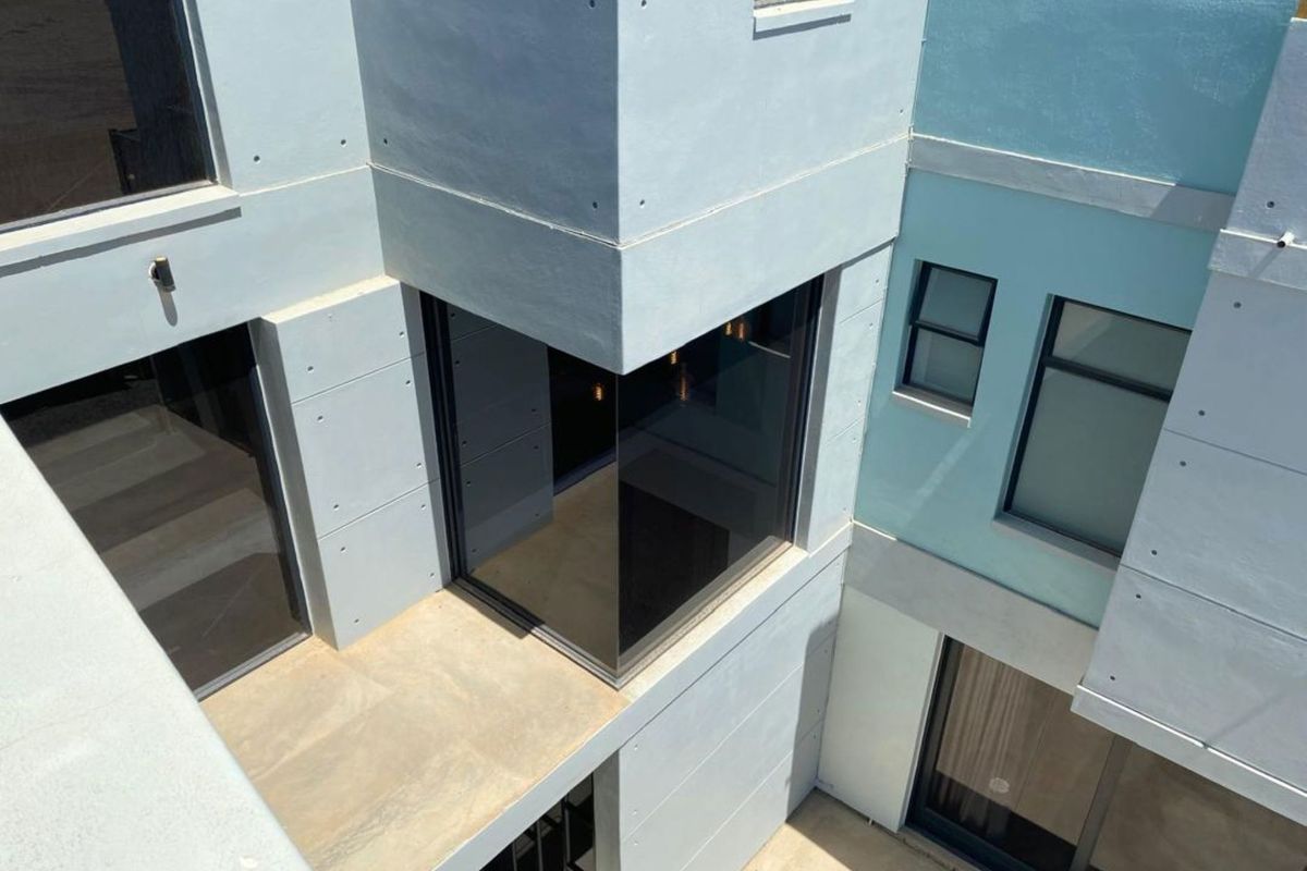 An elevated view of a modern architectural exterior featuring clean lines, concrete-style paneling, and large glass windows.